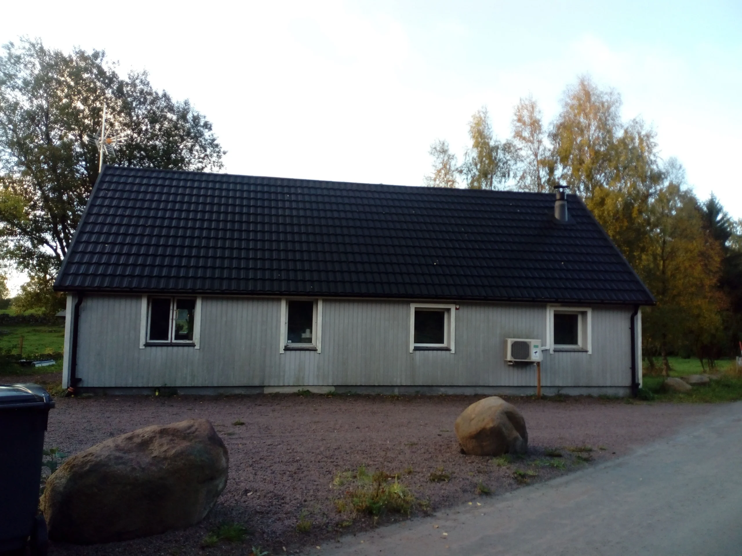 Enkel grå byggnad med svart tak och omgivande stenar